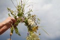 Hands of woman crafting the wreath of wildflowers on a blue cloudy sky