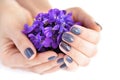 Hands of a woman with dark manicure on nails and bouquet of violets on a white background