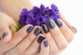 Hands of a woman with dark manicure on nails and bouquet of violets on a white background Royalty Free Stock Photo