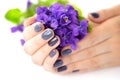 Hands of a woman with dark manicure on nails and bouquet of violets on a white background Royalty Free Stock Photo