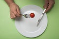 hands of woman eating one cherry tomato in her white plate on green background - Dieting concept Royalty Free Stock Photo