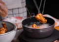 Hands of a woman in gloves are frying the marinated chicken in hot oil in a pan on the kitchen stove and tong the cooked chicken Royalty Free Stock Photo