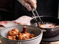 Hands of a woman in gloves are frying the marinated chicken in hot oil in a pan on the kitchen stove and tong the cooked chicken Royalty Free Stock Photo