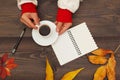 Hands of woman hold a cup of coffee at a wooden table with notebook and pen and autumn leaves Royalty Free Stock Photo