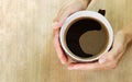 Hands of a woman holding a large cup of coffee. Wooden background. Top view. Copy space Royalty Free Stock Photo