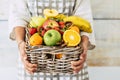 Hands of woman holding wicker basket full of colorful mixed fruit in abundance. Woman with variety of healthy fruit in basket.