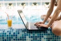 hands of a woman manager typing text on a laptop keyboard sitting by a swimming pool with clear water at a resort on Royalty Free Stock Photo