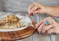 Hands of a woman with manicure and ring with diamonds and blue topaz eating fillet of white fish with risotto