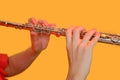 Hands of a woman musician with a flute on a studio yellow background. Flutist with a large concert transverse flute, close up