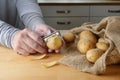 Hands of a woman are peeling raw potatoes with an old peeler on a wooden kitchen table