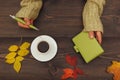 Hands of woman with a pen and notebook at a wooden table with cup of coffee and autumn leaves Royalty Free Stock Photo