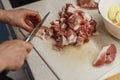 Hands of a woman in process of slicing raw meat on a plastic cutting board