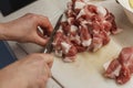 Hands of a woman in process of slicing raw meat on a plastic cutting board