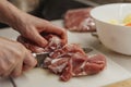 Hands of a woman in process of slicing raw meat on a plastic cutting board