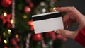 Hands of a woman in a red sweater with a credit card on the background of a Christmas tree close-up. Christmas and New Year Royalty Free Stock Photo