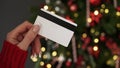 Hands of a woman in a red sweater with a credit card on the background of a Christmas tree close-up. Christmas and New Year Royalty Free Stock Photo