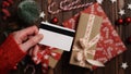 Hands of a woman in a red sweater with a credit card on a background of gift boxes, selective focus, close-up. Christmas and New Royalty Free Stock Photo