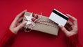 Hands of woman in red sweater holding credit card and gift box on red background close-up,top view,flat lay,copy space.Christmas Royalty Free Stock Photo