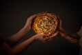 Hands of a man and a woman holding a wreath of branches with yellow Christmas lights around a black background