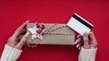 Hands of woman in white sweater holding credit card and gift box on red background close-up,top view,flat lay,copy space.Christmas Royalty Free Stock Photo