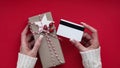 Hands of woman in white sweater holding credit card and gift box on red background close-up,top view,flat lay,copy space.Christmas Royalty Free Stock Photo