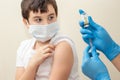 Hands of women in blue gloves with a syringe injecting a vaccine to a boy in a medical mask