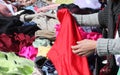 Hands of women trying a red dress in the stall with many items of clothing for sale