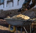 Hands in work gloves throw sawdust on a one wheeled cart