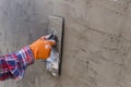 The hands of a worker who are plastering up close are wearing orange rubber gloves to prevent the cement from biting their hands,