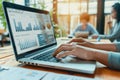 hands working at a laptop with charts on the screen, in background blurry people working at laptop Royalty Free Stock Photo