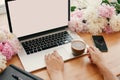 Hands working on stylish laptop with empty screen, coffee, phone, black notebook and peonies on rustic wooden table. Freelance Royalty Free Stock Photo