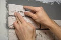 Hands working tiler in the process of laying plaster tiles on the wall of the room. Repair of apartments