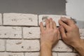 Hands working tiler in the process of laying plaster tiles on the wall of the room. Repair of apartments