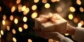 Hands wrapping a ribbon on a gift box in front of a christmas tree with warm lights Royalty Free Stock Photo