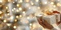 Hands wrapping a ribbon on a gift box in front of a christmas tree with warm lights Royalty Free Stock Photo