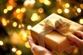 Hands wrapping a ribbon on a gift box in front of a christmas tree with warm lights Royalty Free Stock Photo