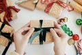 Hands wrapping stylish christmas gift. Person preparing modern gift box with green ribbon, golden wrapping paper, ornaments on Royalty Free Stock Photo
