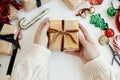 Hands wrapping stylish christmas gift. Person preparing modern gift box with velvet ribbon, golden wrapping paper, ornaments on Royalty Free Stock Photo