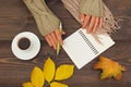 Hands of writer with a pen and notebook at a wooden table with cup of espresso and autumn leaves and scarf Royalty Free Stock Photo