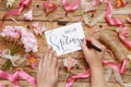 Hands Writing romantic HELLO SPRING card between pink flowers