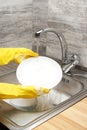 Hands in yellow gloves washing plate against kitchen sink Royalty Free Stock Photo