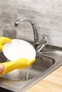 Hands in yellow gloves washing white plate under tap water Royalty Free Stock Photo