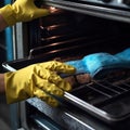 hands in yellow household gloves clean the oven