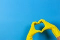 Hands in yellow rubber gloves making heart shape with fingers, on blue background Royalty Free Stock Photo