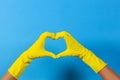 Hands in yellow rubber gloves making heart shape with fingers, on blue background Royalty Free Stock Photo