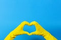 Hands in yellow rubber gloves making heart shape with fingers, on blue background Royalty Free Stock Photo