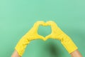 Hands in yellow rubber gloves making heart shape with fingers, on green background Royalty Free Stock Photo