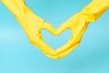 Hands in yellow rubber gloves in the shape of a heart on blue background