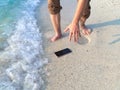 Hands of young Asian man dropping mobile smart phone on tropical sandy beach. Accident and insurance electronic equipment concept Royalty Free Stock Photo