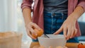 Hands of young Asian woman chef cracking eggs into ceramic bowl cooking omelette with vegetables on wooden board on kitchen table Royalty Free Stock Photo